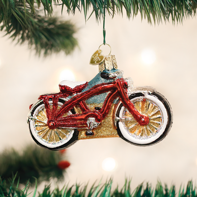 Red and gold glass cruiser bike ornament hanging on a Christmas tree branch.