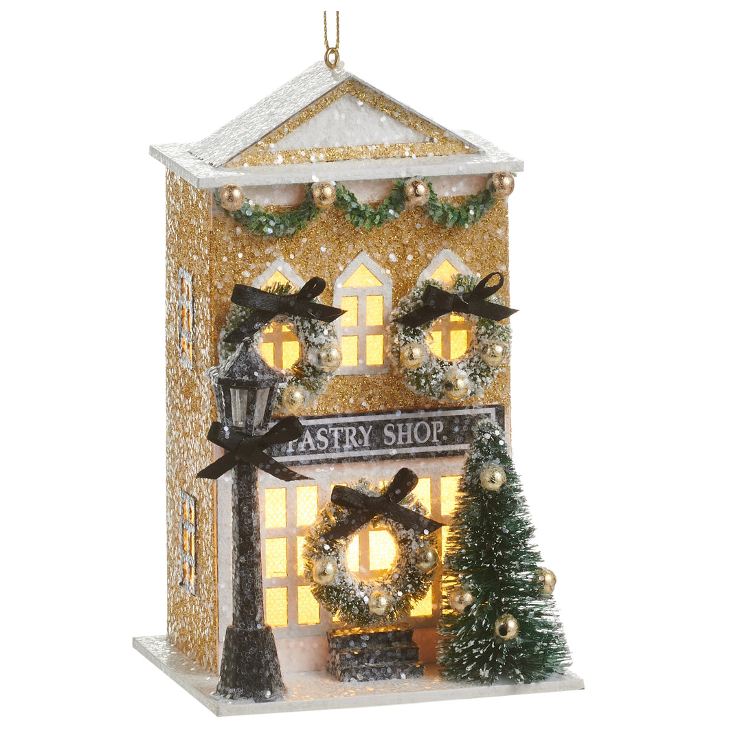 Lighted gold glitter pastry shop ornament with wreaths, a lamp post, and a small sisal tree.