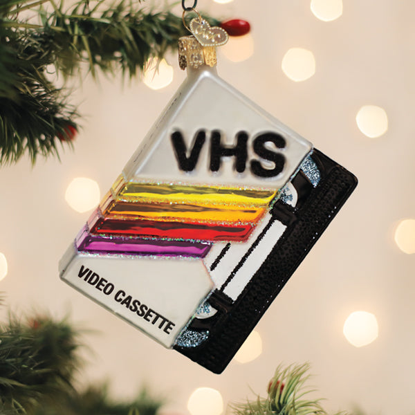 Glass VHS tape Christmas ornament with retro rainbow stripes hanging on a tree.