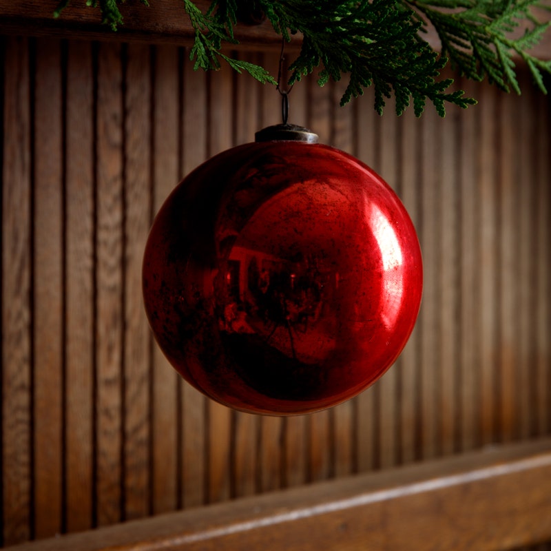 Vintage 6-inch red glass ball ornament with an antique mercury finish hanging from a green branch.