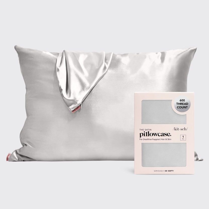 A silver satin pillowcase displayed next to its pink and white 600 thread count packaging.