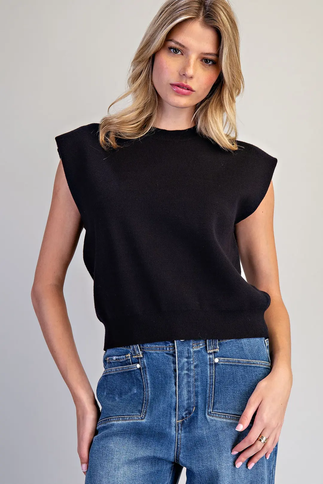 Woman wearing the Elle black sleeveless knit top with extended shoulders and blue jeans.