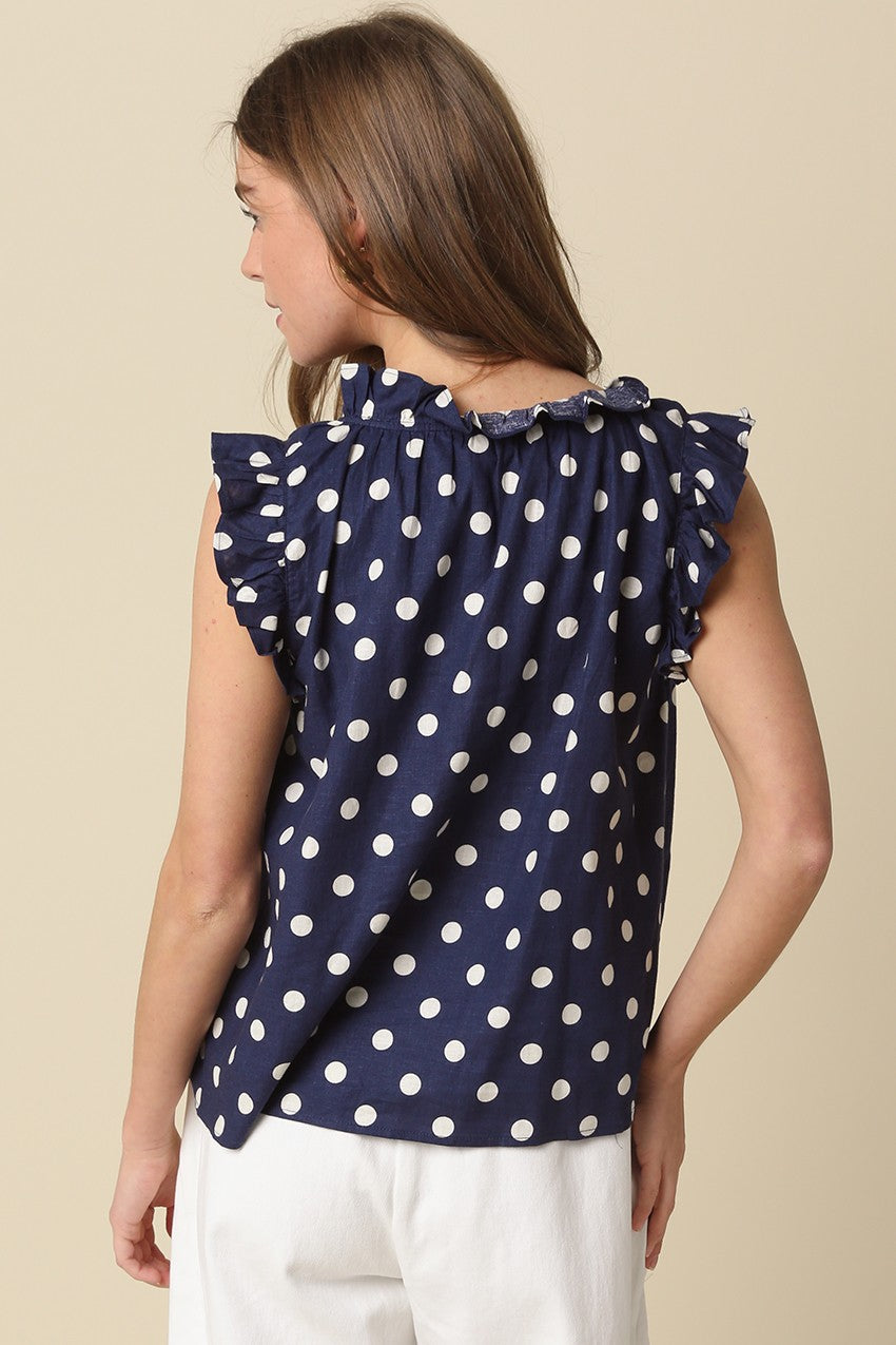 Back view of a navy blue sleeveless blouse with white polka dots and ruffle trim on the collar.
