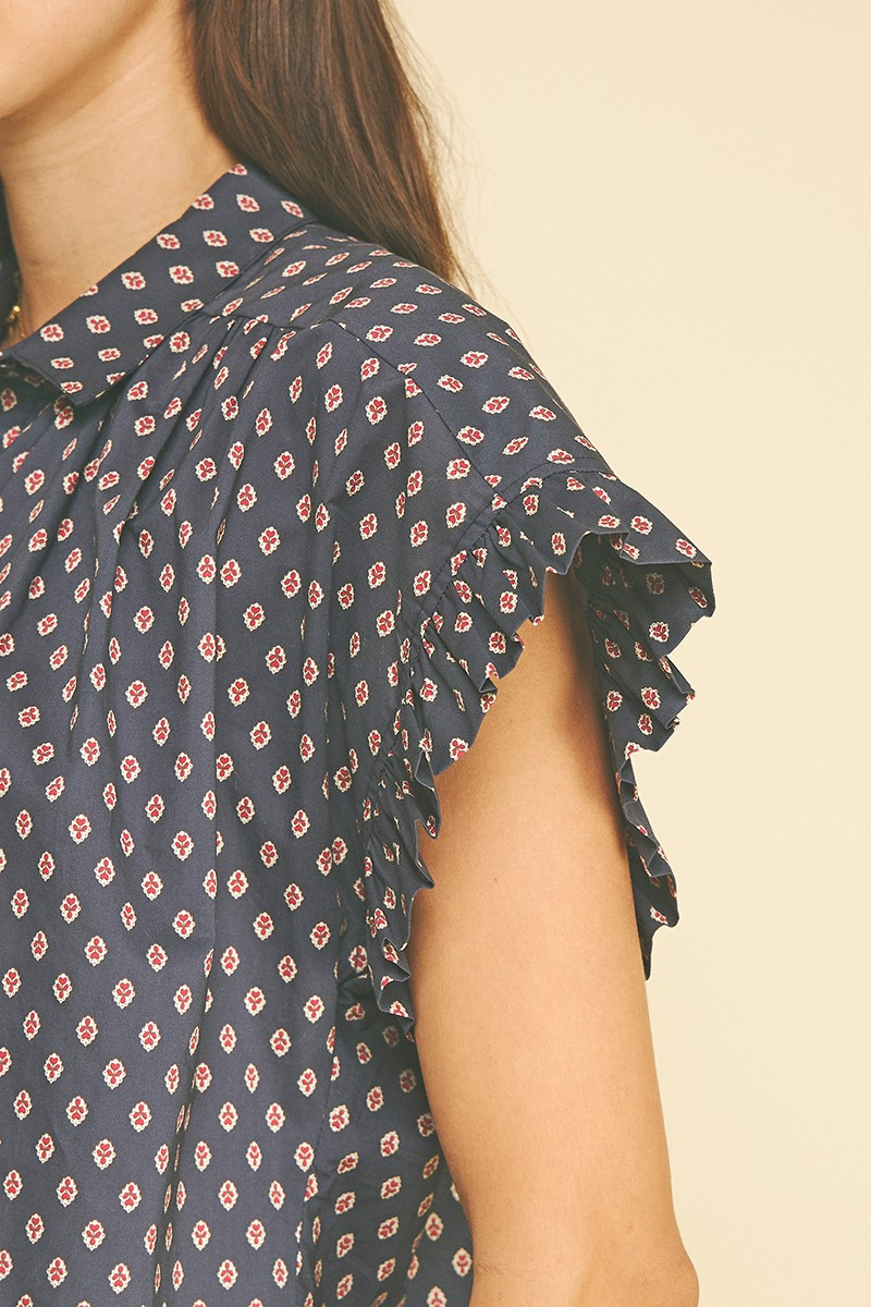 Close-up of the Emiliana shirt featuring a navy geometric diamond print and ruffled cap sleeves.