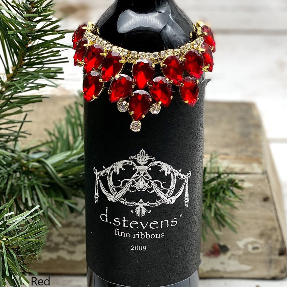 Princess pear-shaped red crystal wine collar with gold settings on a black wine bottle.