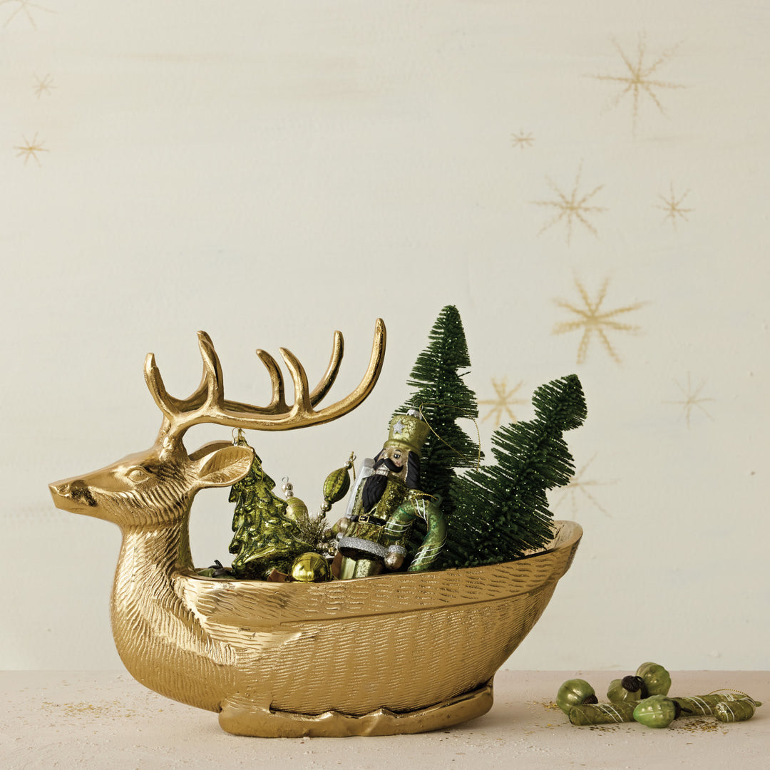 Gold finish cast aluminum reindeer shaped bowl filled with green Christmas ornaments and trees.