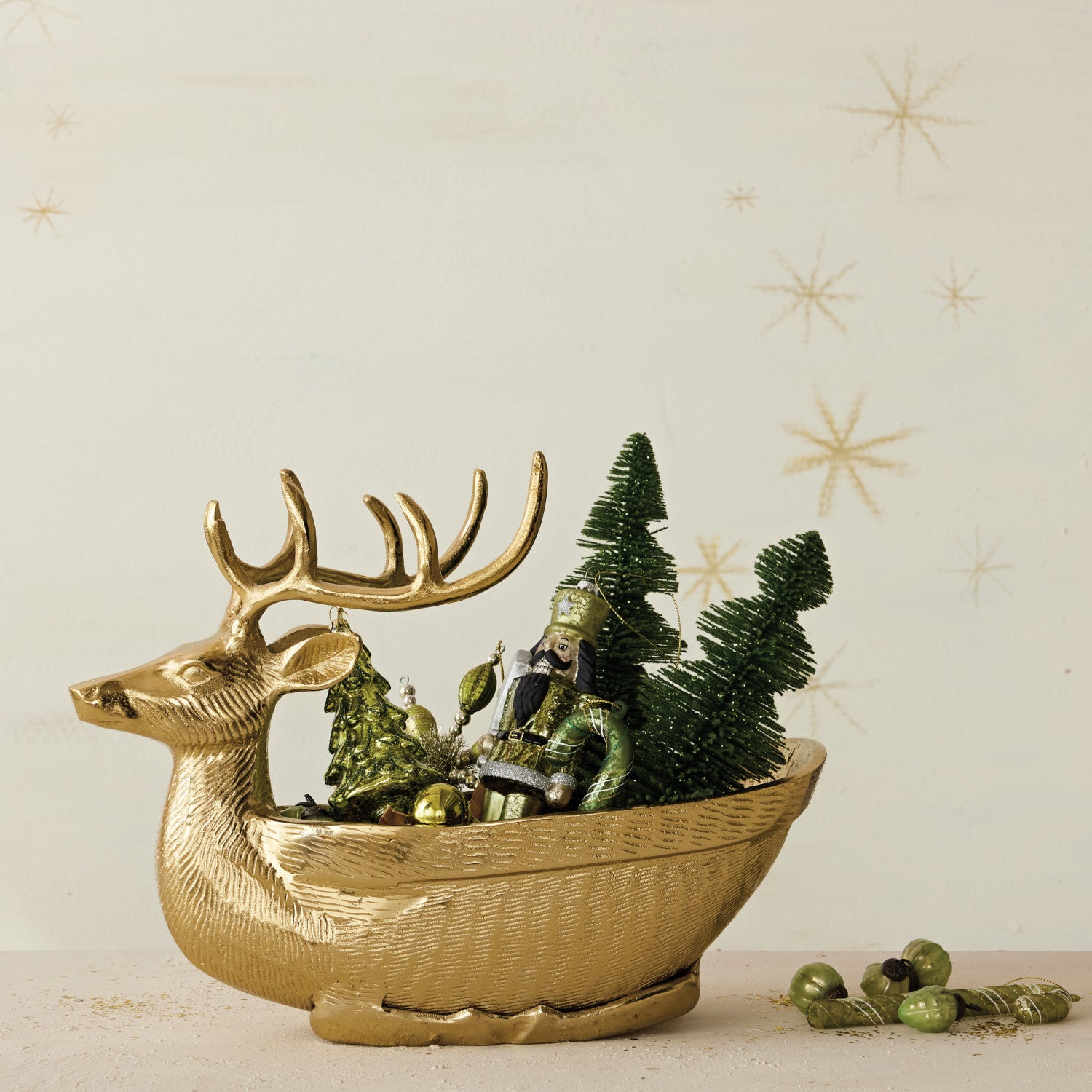 Gold finish cast aluminum reindeer shaped bowl filled with green Christmas ornaments and trees.
