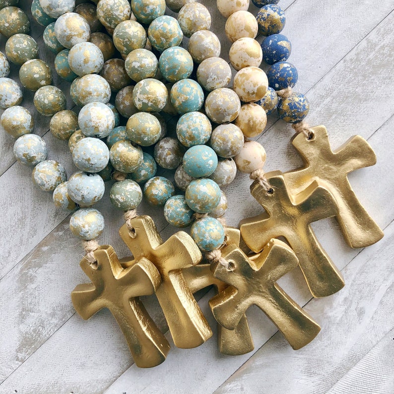 Handmade gold enameled clay cross blessing bead hanging from a doorknob.