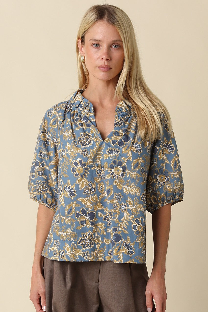 Woman wearing a Marina Floral Puff Sleeve Blouse in blue with a yellow and white floral pattern.