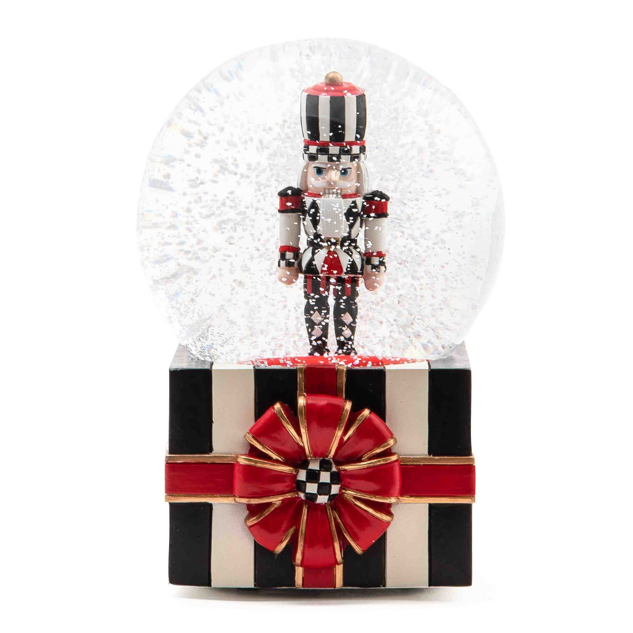 Resin nutcracker snow globe with striped gift box base, red ribbon, and Courtly Check ball pattern.