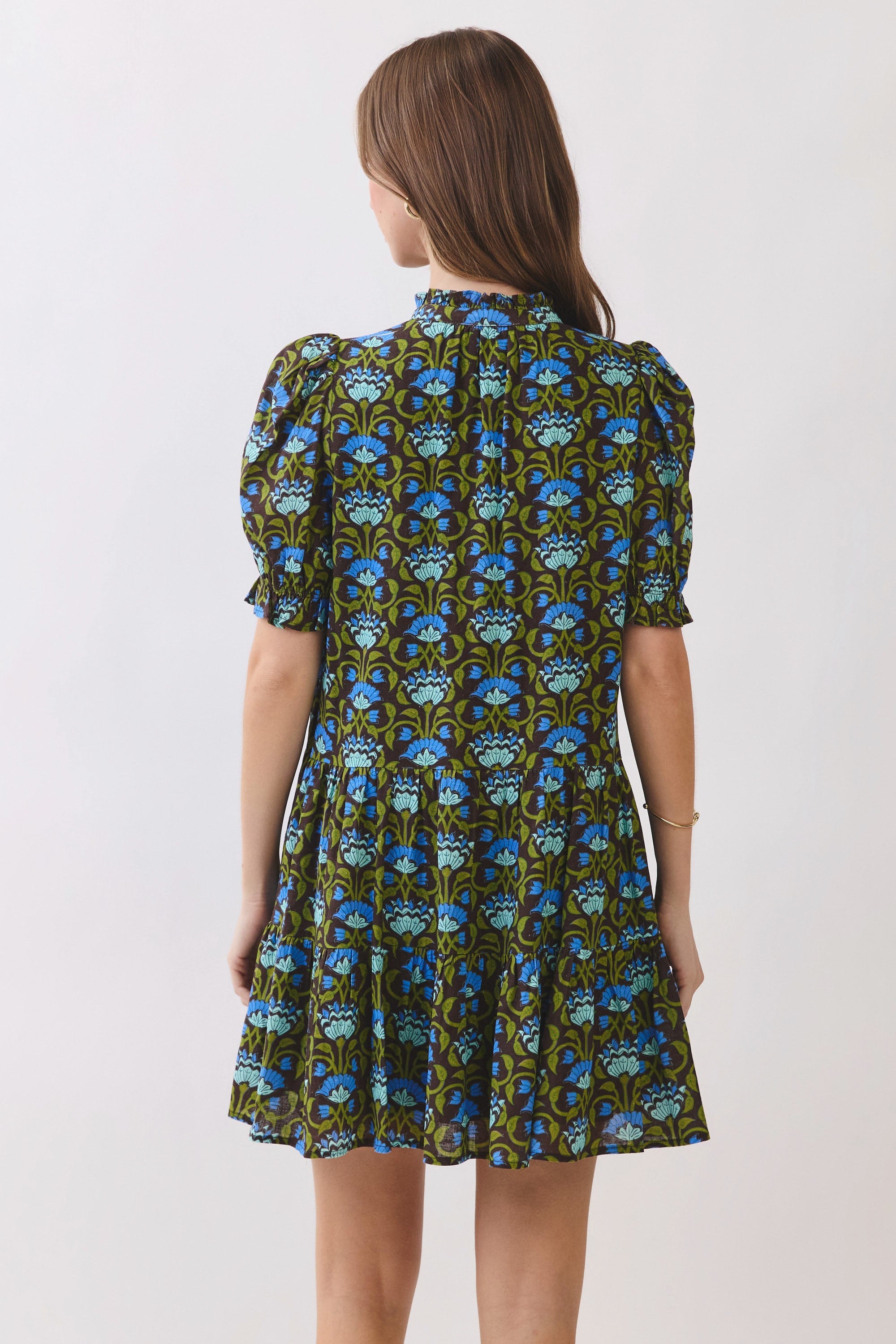 Back view of a tiered floral print mini dress with short puff sleeves and a high ruffle neckline.