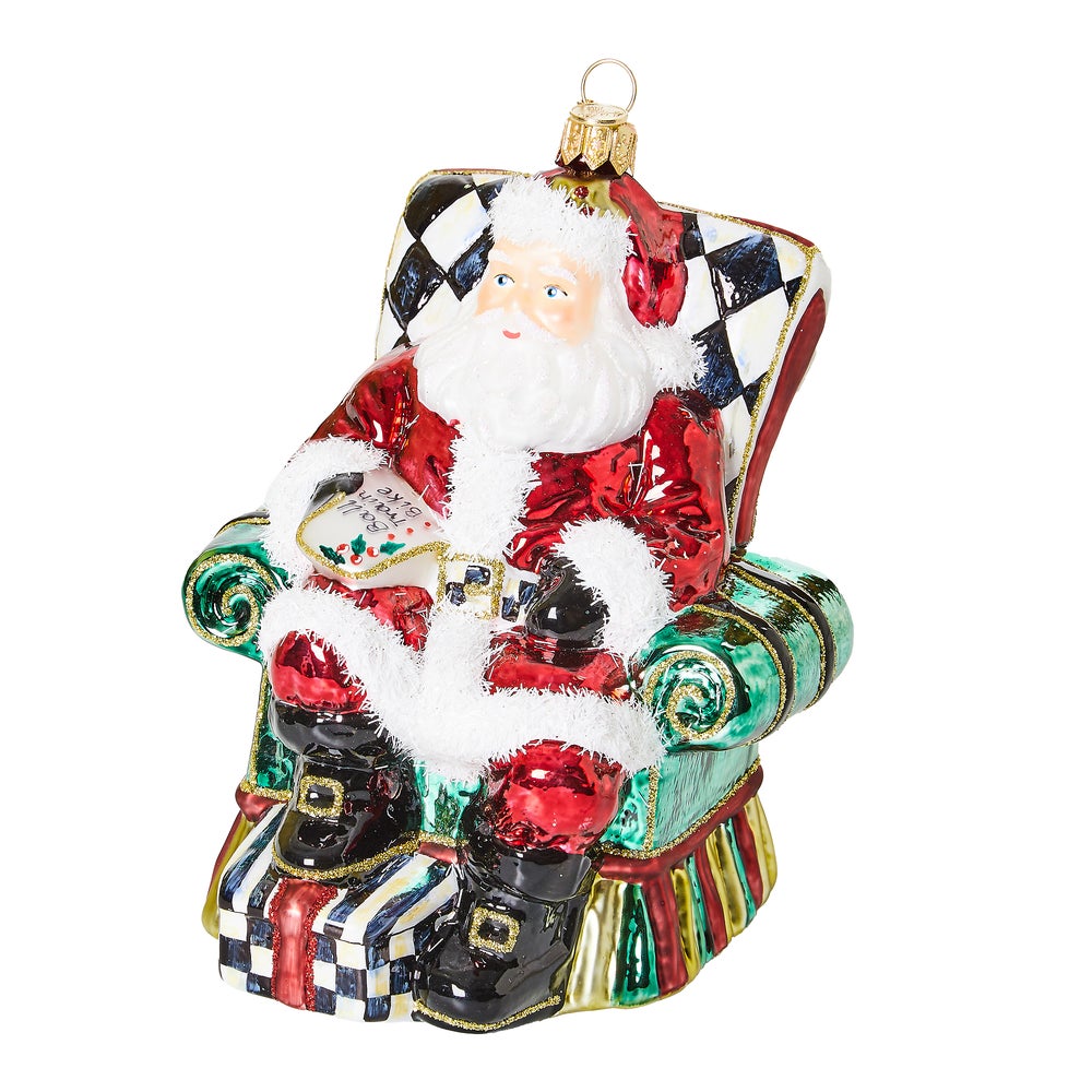 Hand-painted glass Santa ornament sitting in a checkered chair holding a wish list.