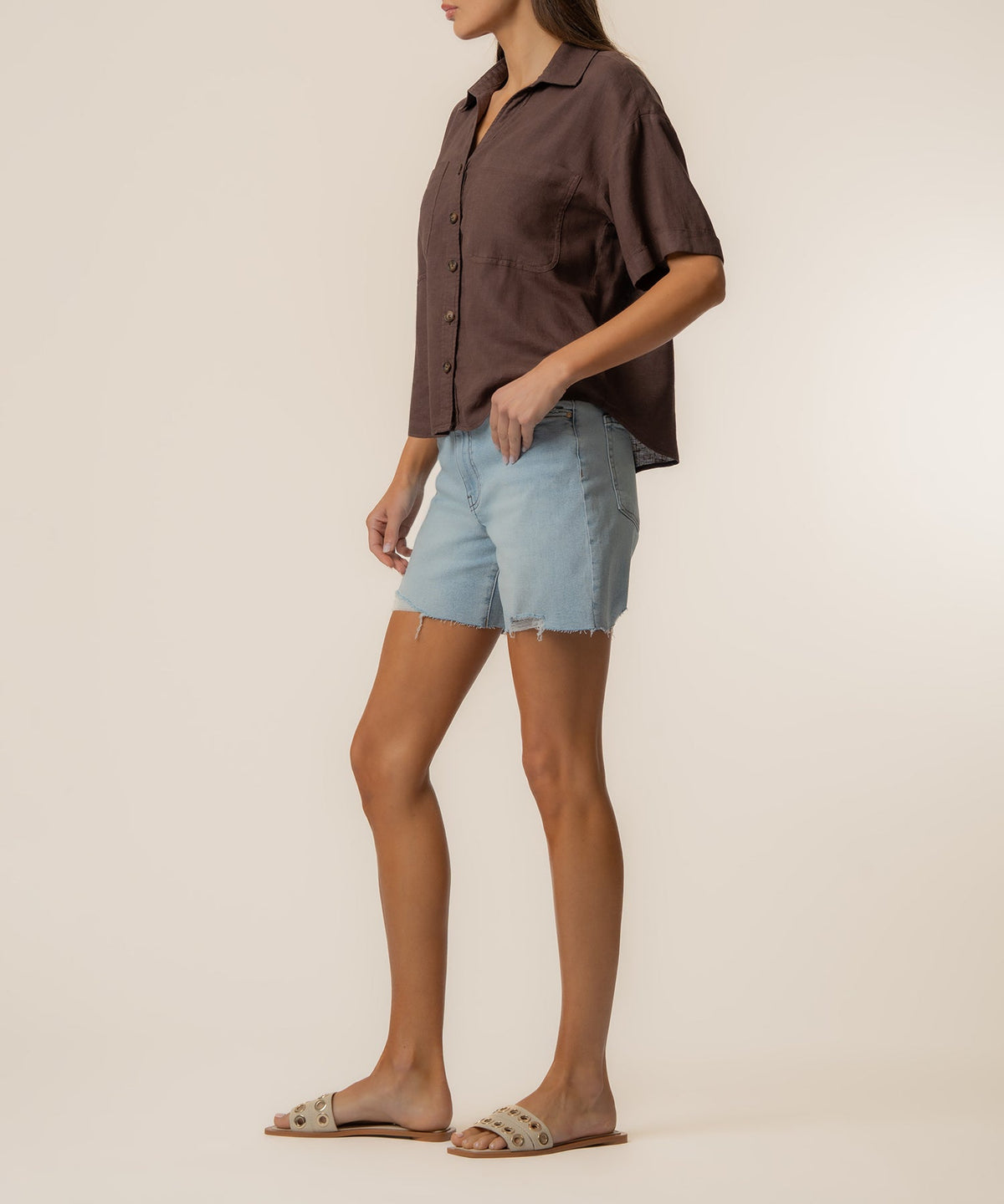 Woman wearing a brown Brianna Linen Boxy Shirt with light wash denim shorts and tan sandals.