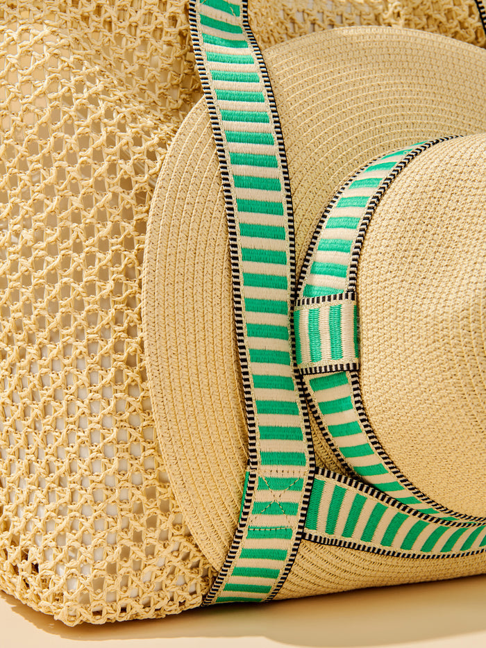 Open-weave paper straw tote with bold striped shoulder straps, magnetic closure, slip pocket, and attached adjustable sun hat.