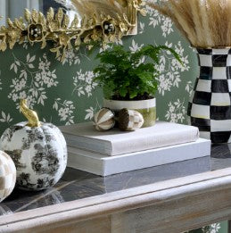 Two Mocha Check Acorns with striped patterns resting on a stack of white books on a console table.