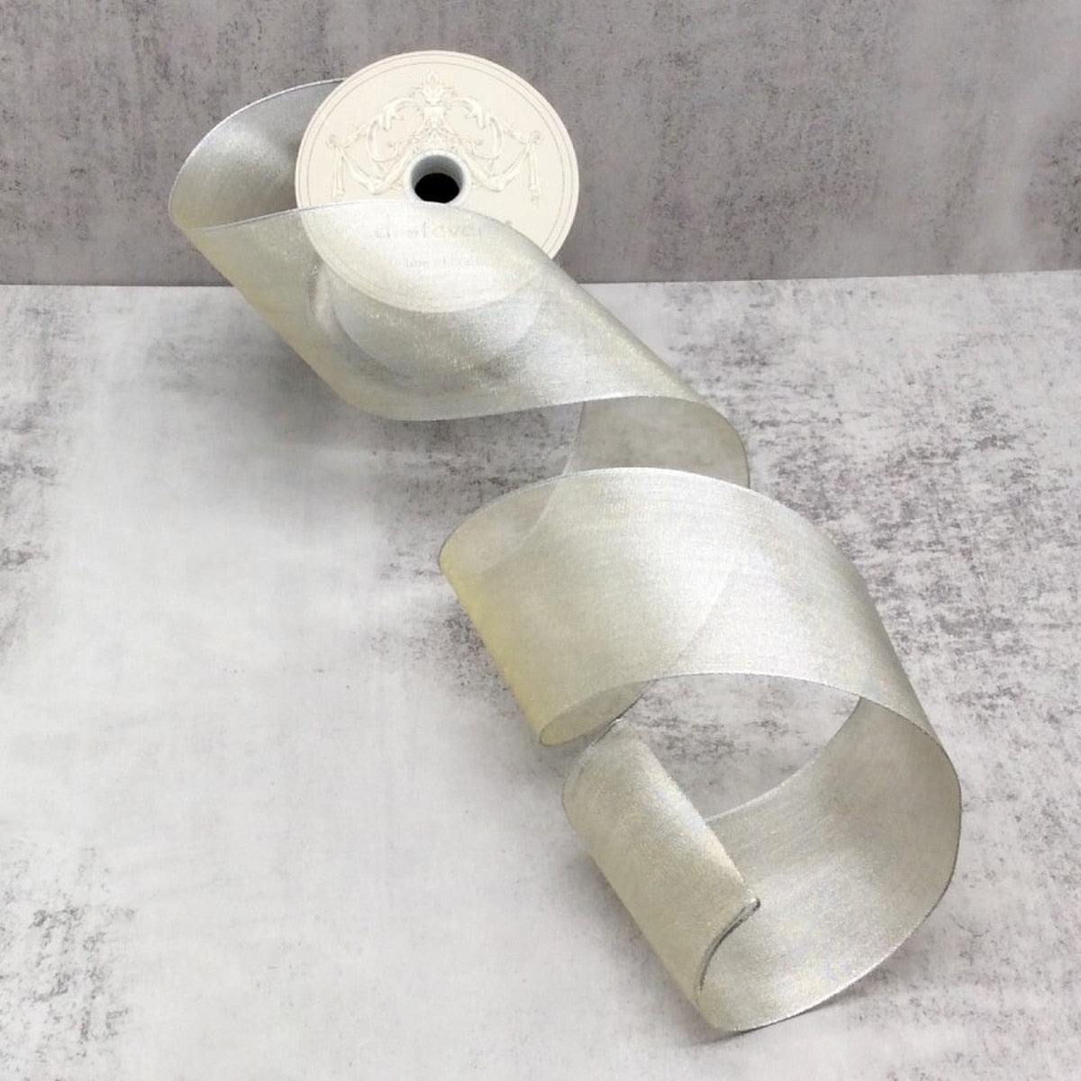 A roll of shimmering silver metallic mesh ribbon on a light gray textured background.