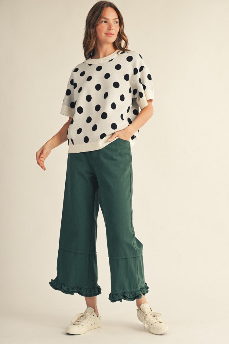 Woman wearing the Emily Polka Dot Comry Sweater Top in cream with large black dots and green pants.