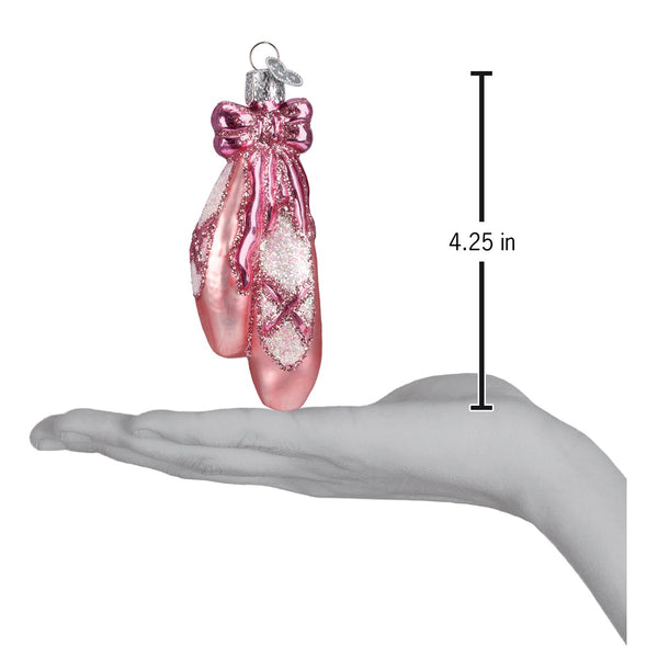 Pink glittery ballet toe shoes ornament shown next to a hand for scale, measuring 4.25 inches tall.
