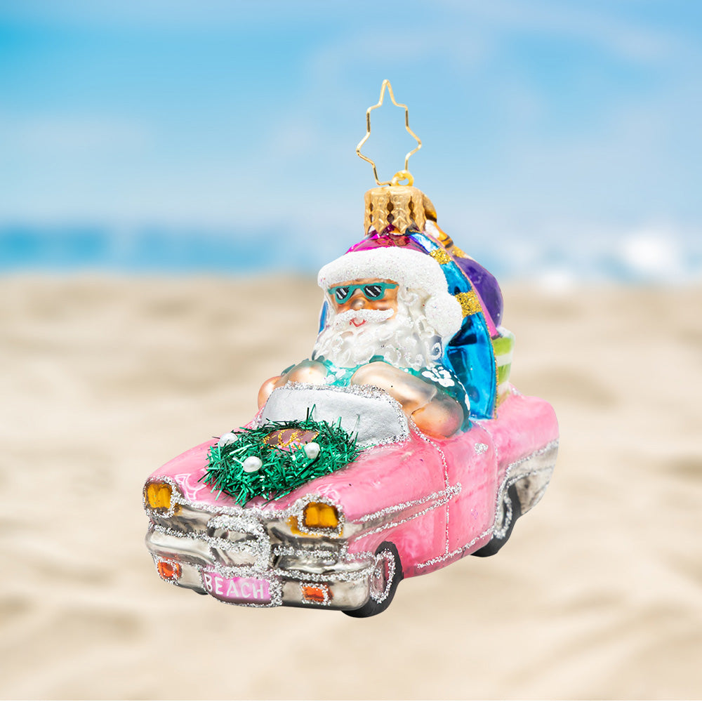 Santa Claus in a pink convertible glass ornament with a surfboard and beach gear.