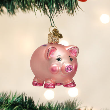 Pink glass piggy bank Christmas ornament with glitter accents hanging on a tree branch.