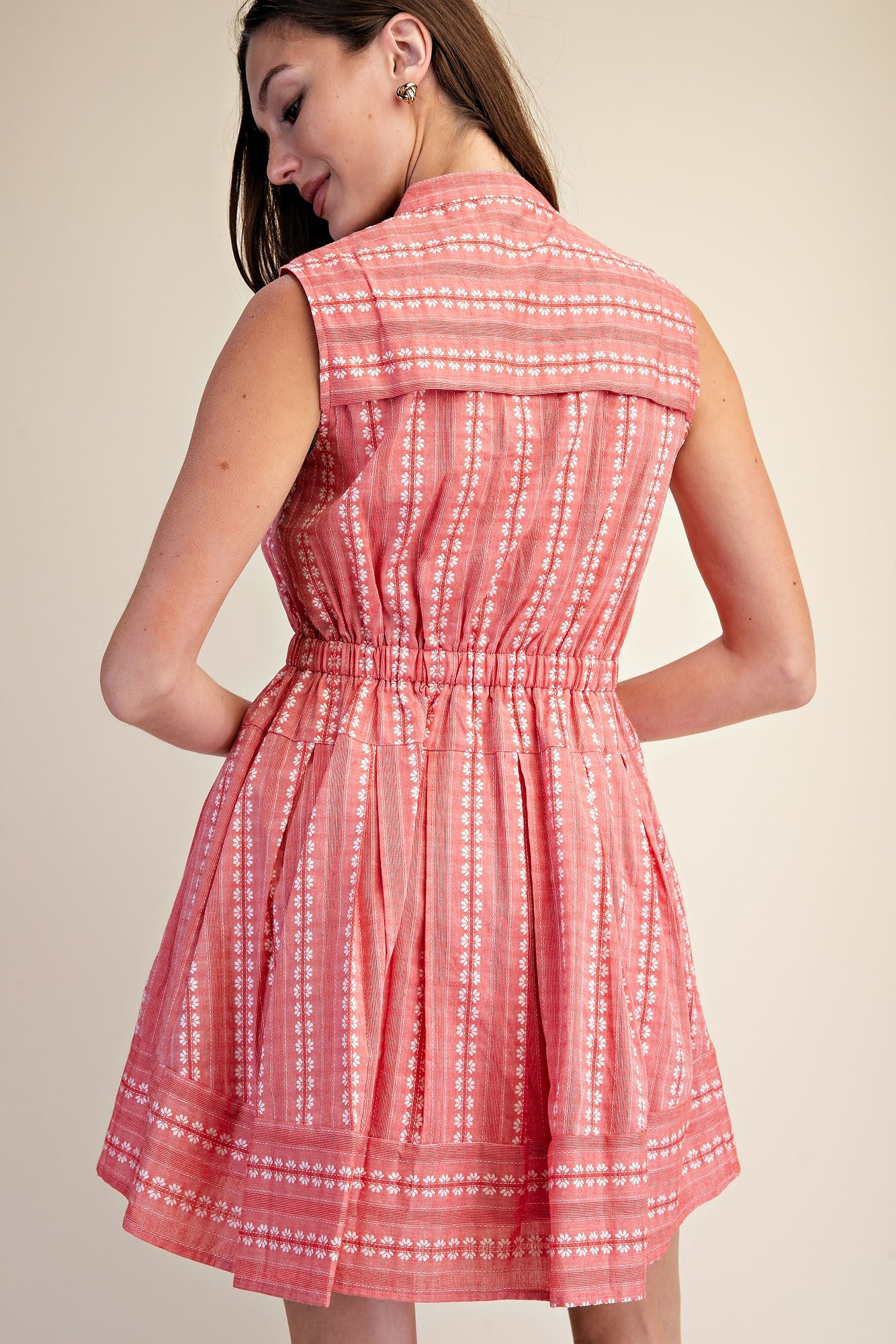 Back view of a sleeveless coral pink boho shirt dress with white floral embroidery and cinched waist