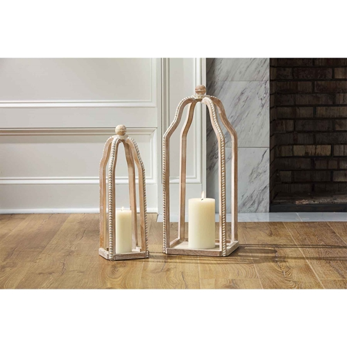 Two tall, light wood lanterns with beaded trim and cream candles inside, set on a wooden floor.
