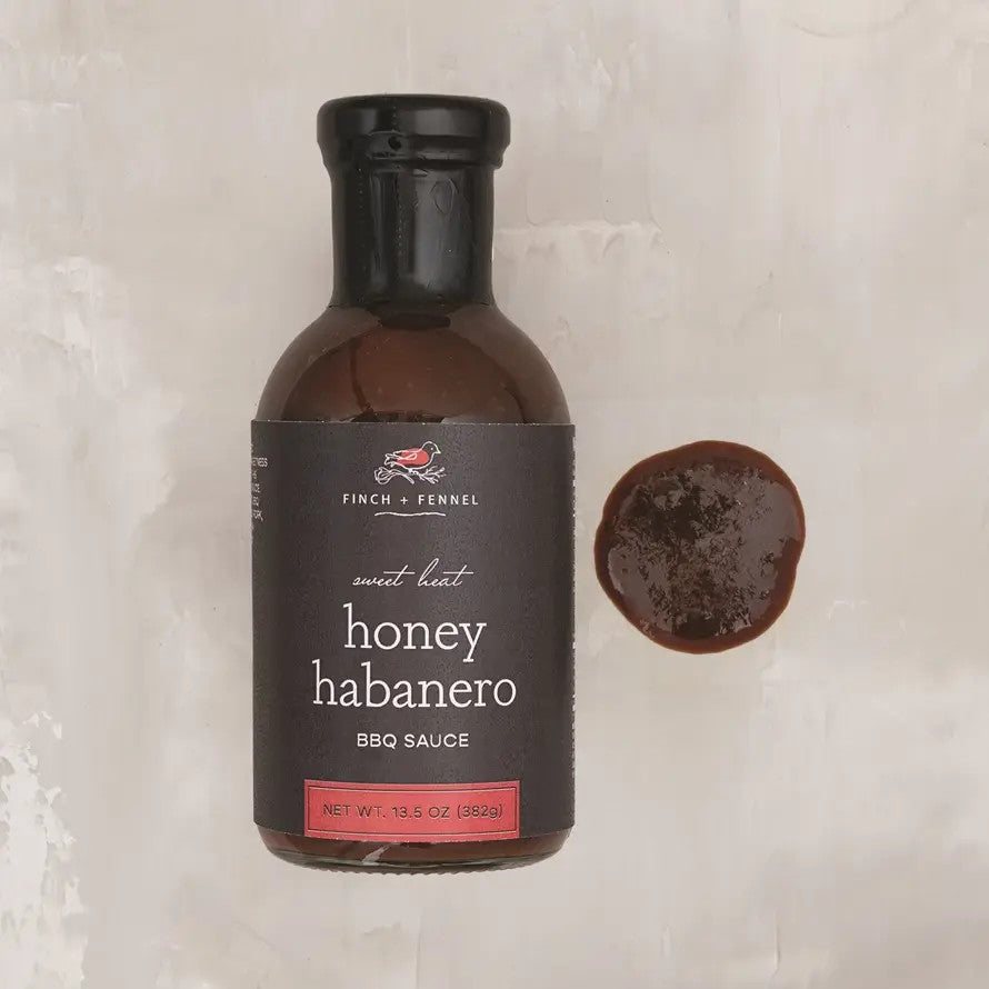 A bottle of Finch + Fennel Honey Habanero BBQ Sauce next to a small pool of the dark brown sauce.