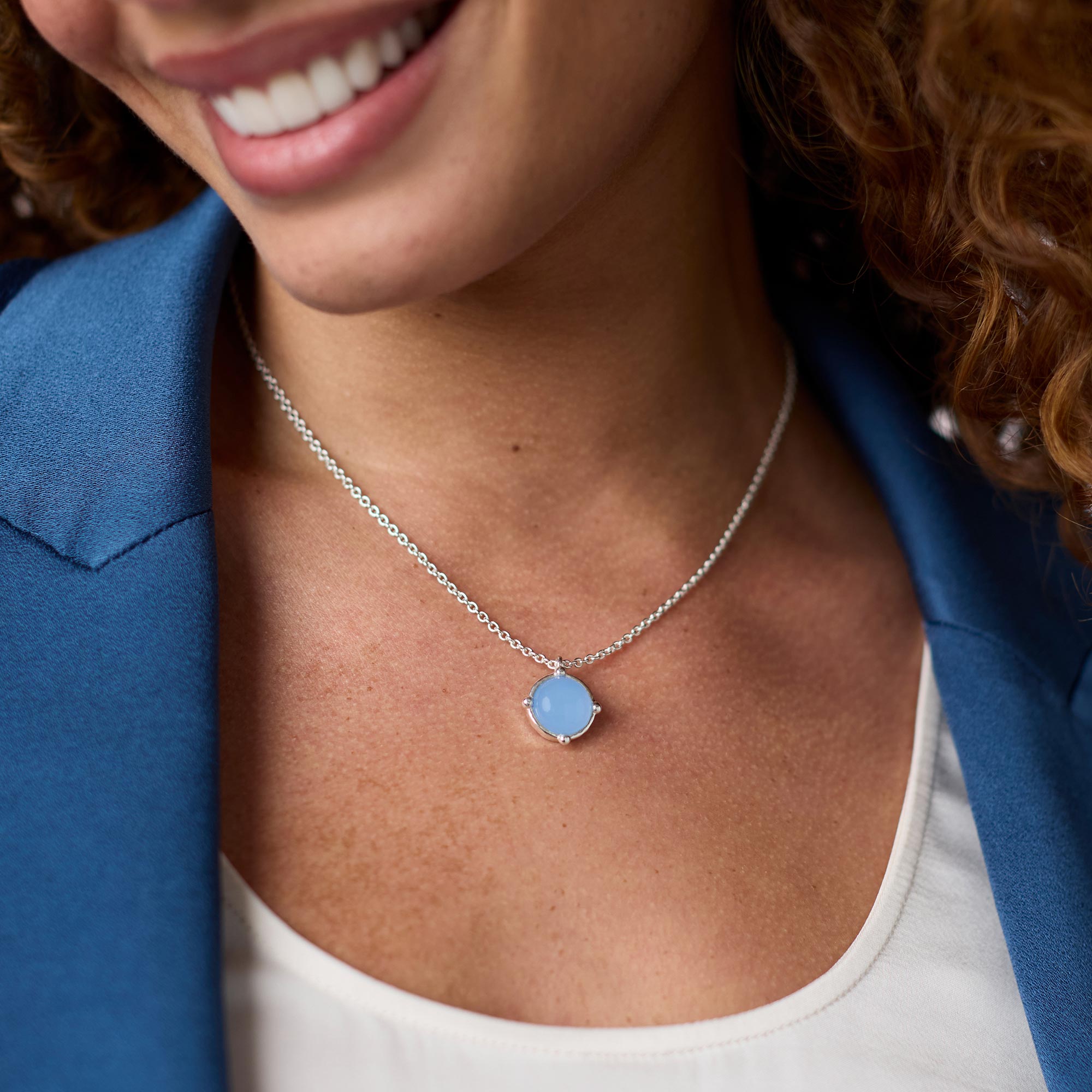 A woman wearing the Honeybee Solitaire Necklace in silver with a round light blue gemstone pendant.