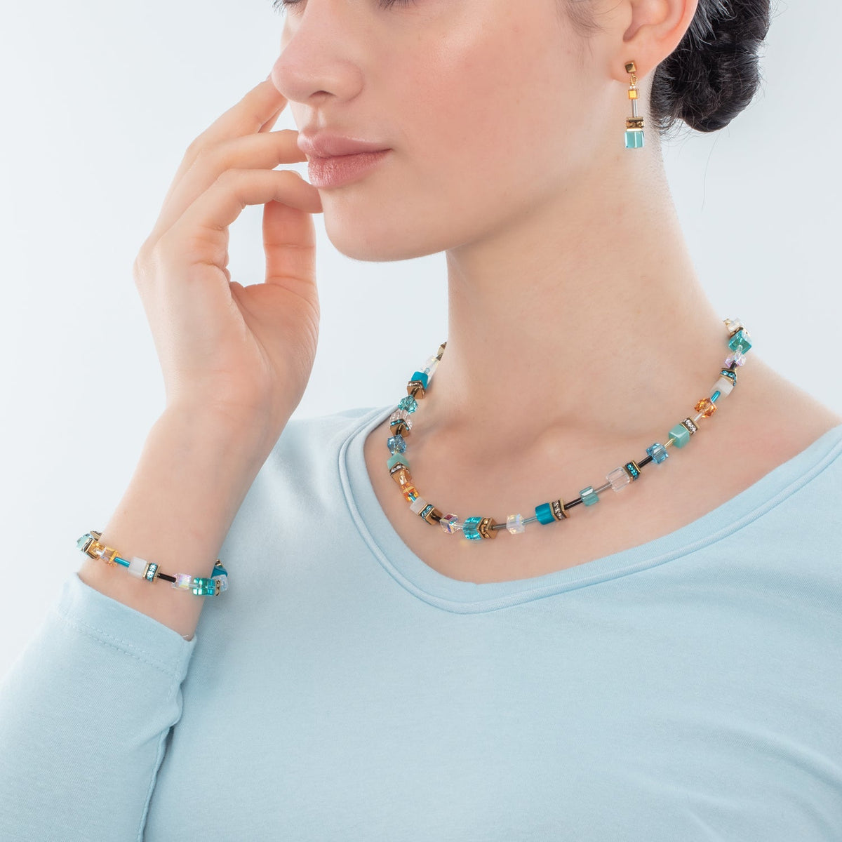 Woman wearing a Geocube Iconic Necklace in gold and turquoise with matching bracelet and earrings.
