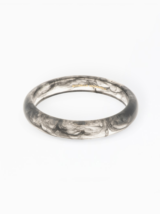 Betty Bangle, a clear resin bracelet with a black smoky swirl pattern and gold interior branding.