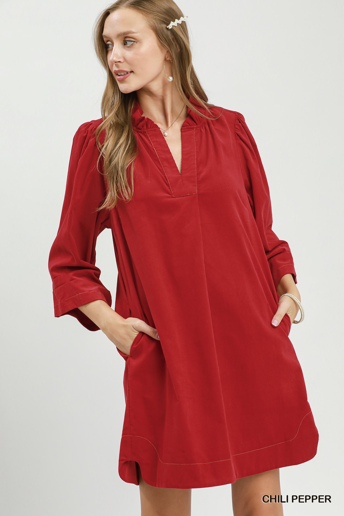 Woman wearing a red corduroy split neck shift dress with puff sleeves and side pockets.