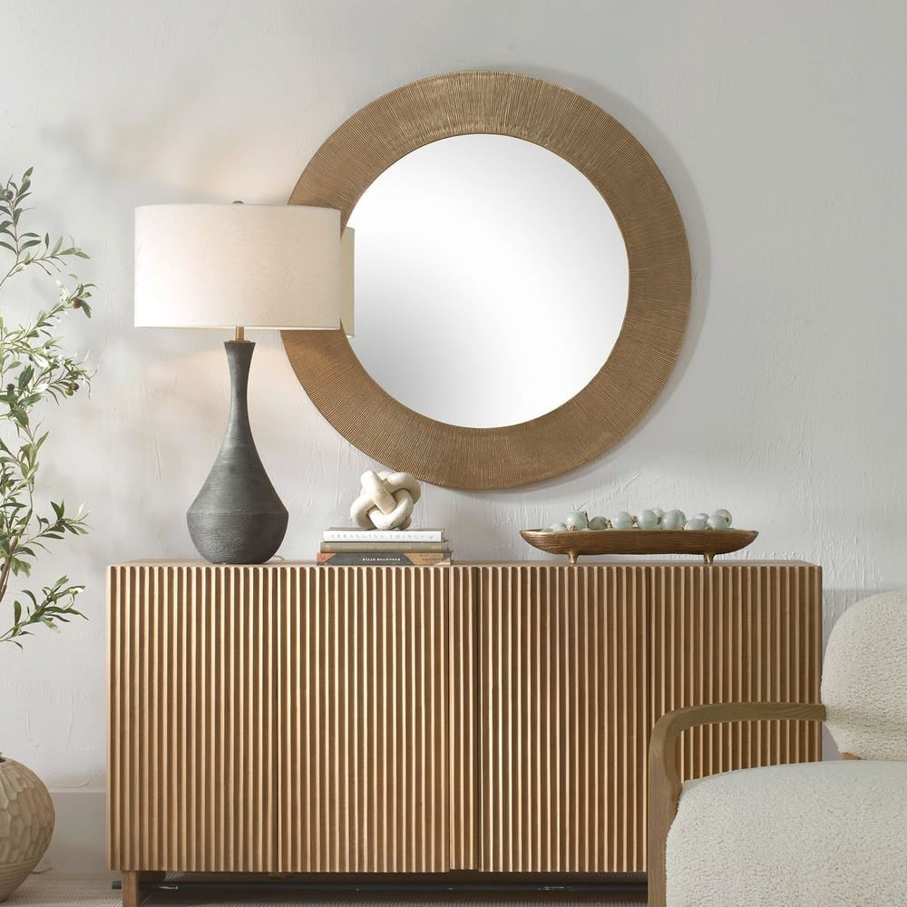 Tano Round Mirror with a textured gold frame hanging above a fluted wood sideboard.