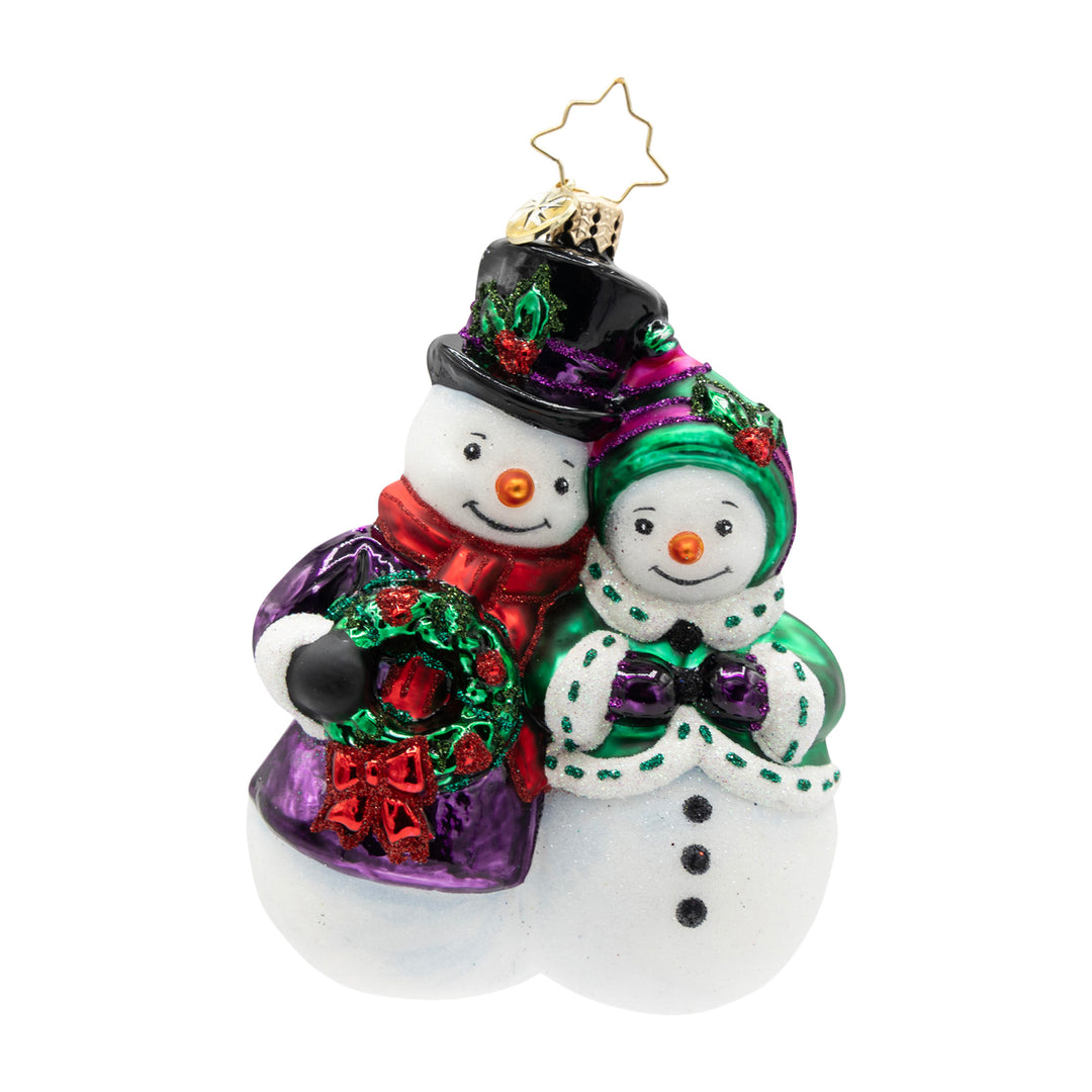 Glass Christmas ornament featuring a snowman couple in festive attire with a wreath and muff.