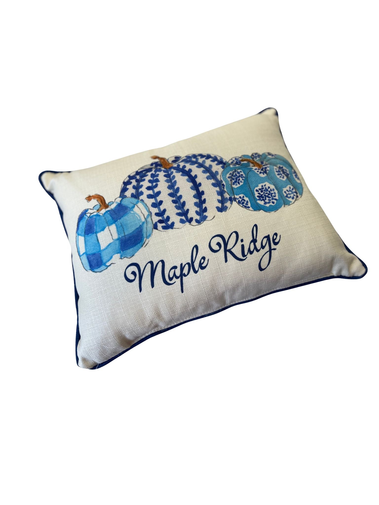 White decorative pillow with blue patterned pumpkins, navy piping, and "Maple Ridge" script.