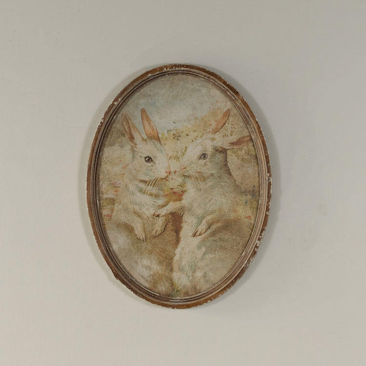 Oval framed duo print featuring two bunny silhouettes on glass over wood.
