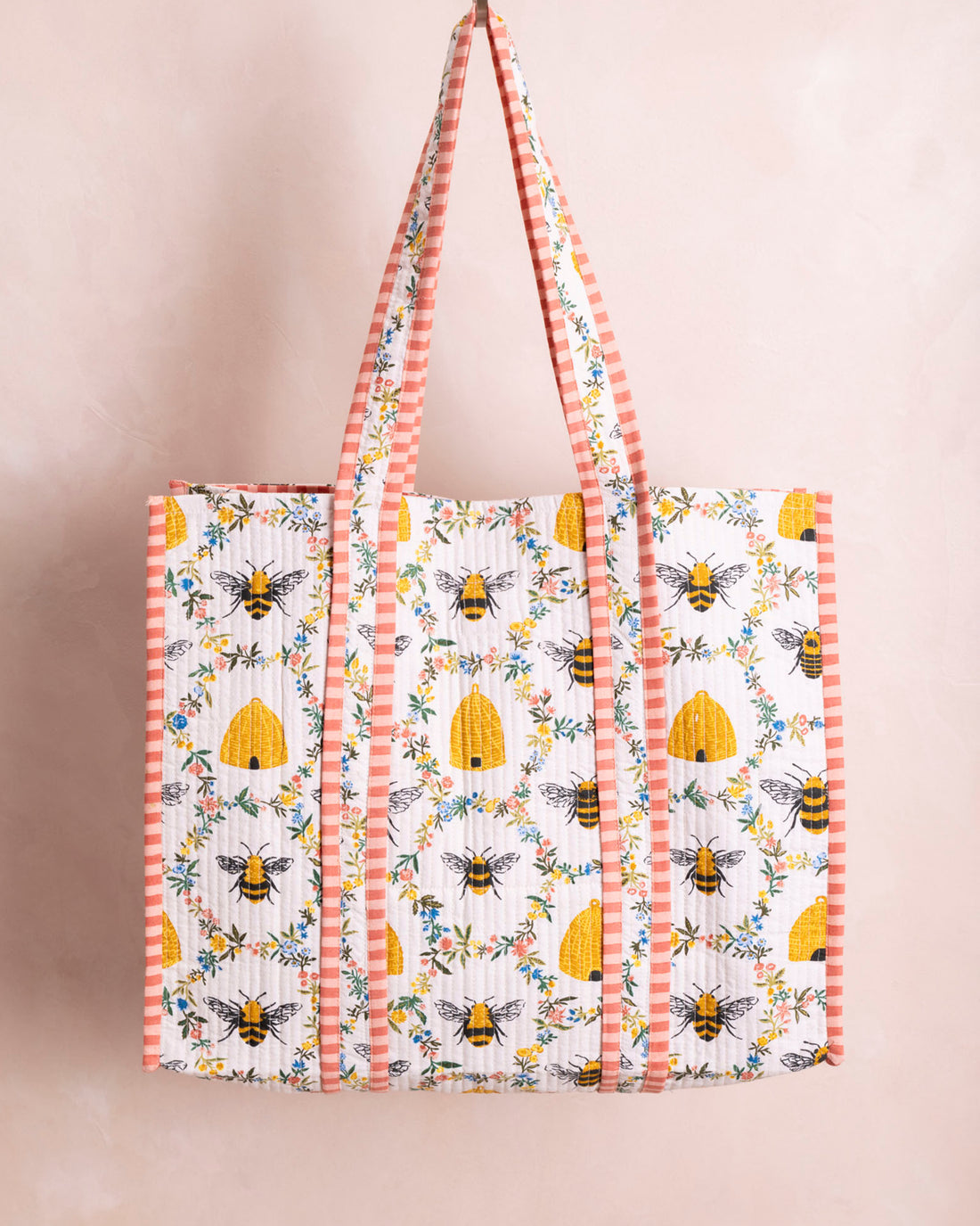 Quilted white tote bag with yellow bee and beehive print, featuring pink striped handles.