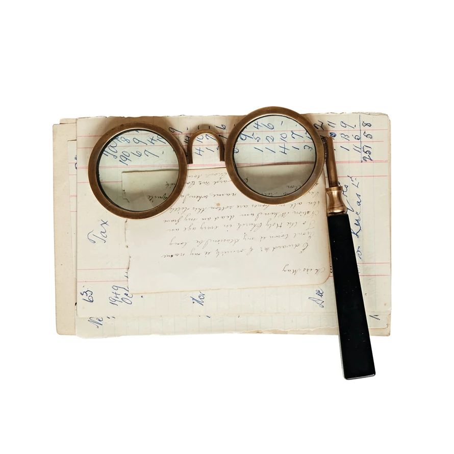 Antique brass spectacle magnifying glass with a black handle resting on vintage handwritten notes.
