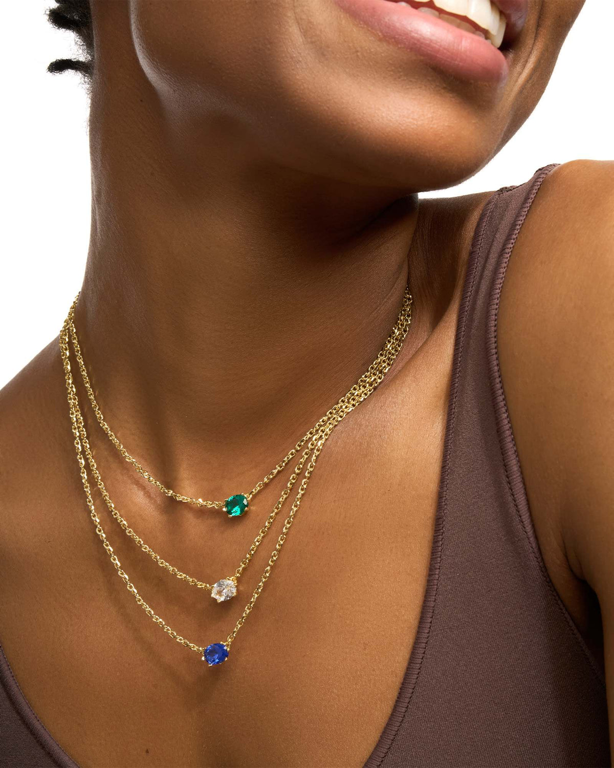Model wearing three Cailin Crystal Pendant Necklaces in green, white, and blue on gold chains.