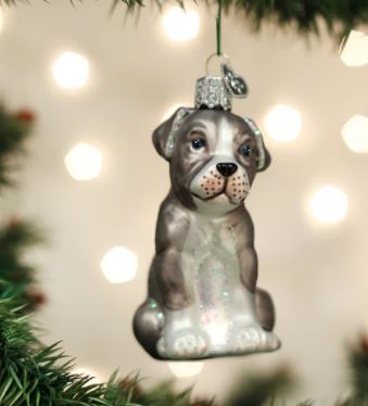 Glass Pitbull Pup ornament hanging on a Christmas tree with a blurred light background.