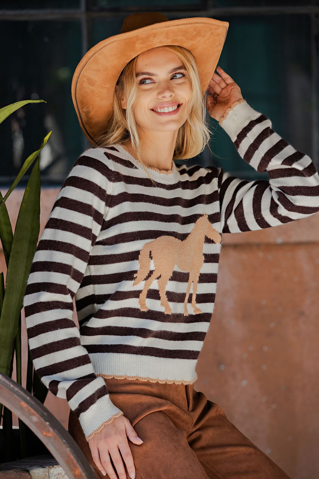 Woman wearing a brown and white striped crewneck sweater with a tan horse graphic and scallop edges.