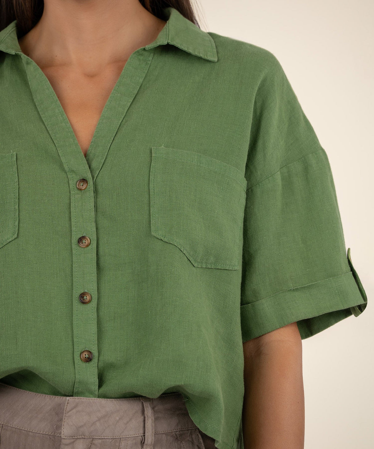 Close-up of a green boxy button-front shirt with short cuffed sleeves and a chest pocket.