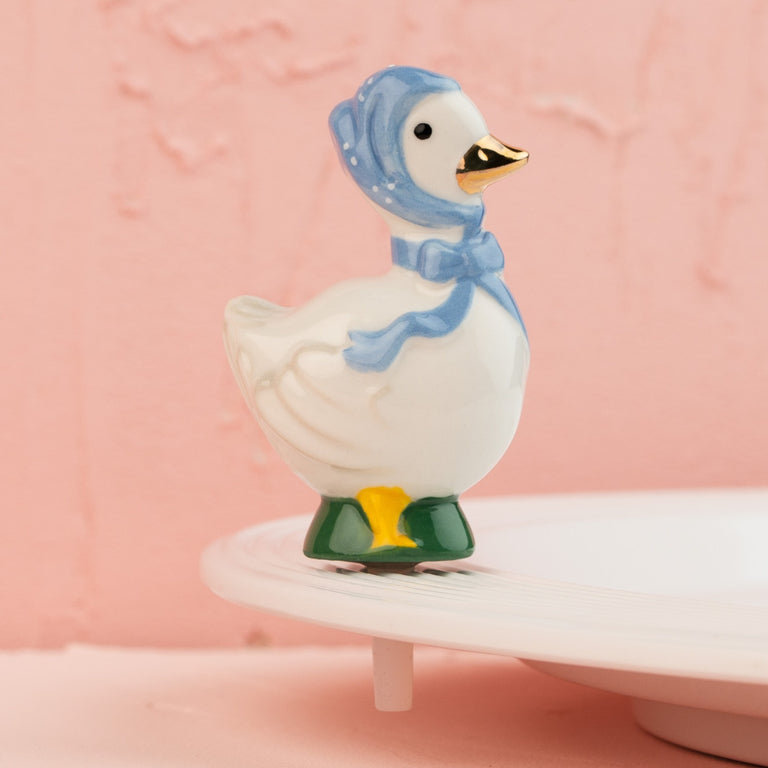 Hand-painted ceramic goose mini wearing a blue bonnet and bow, perched on a white platter.