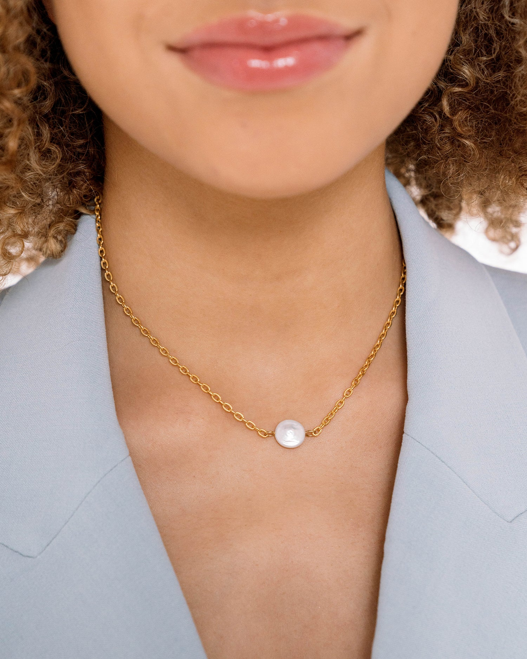 Close-up of a woman wearing a dainty gold chain necklace with a single round white pearl pendant.