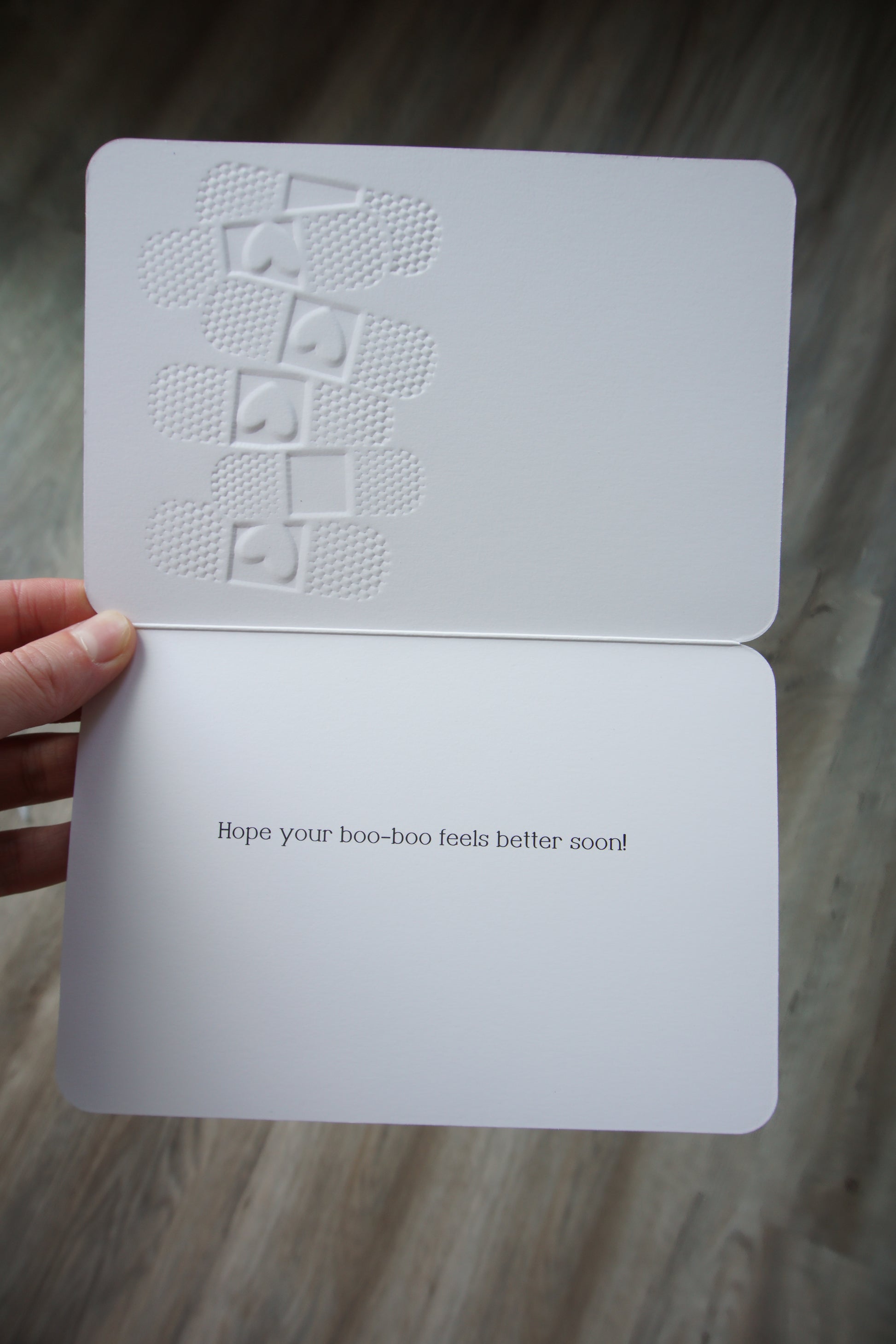 Die-cut get well card shaped like a bandage with embossed texture; outside reads Ouch and inside says Hope your boo-boo feels better soon.