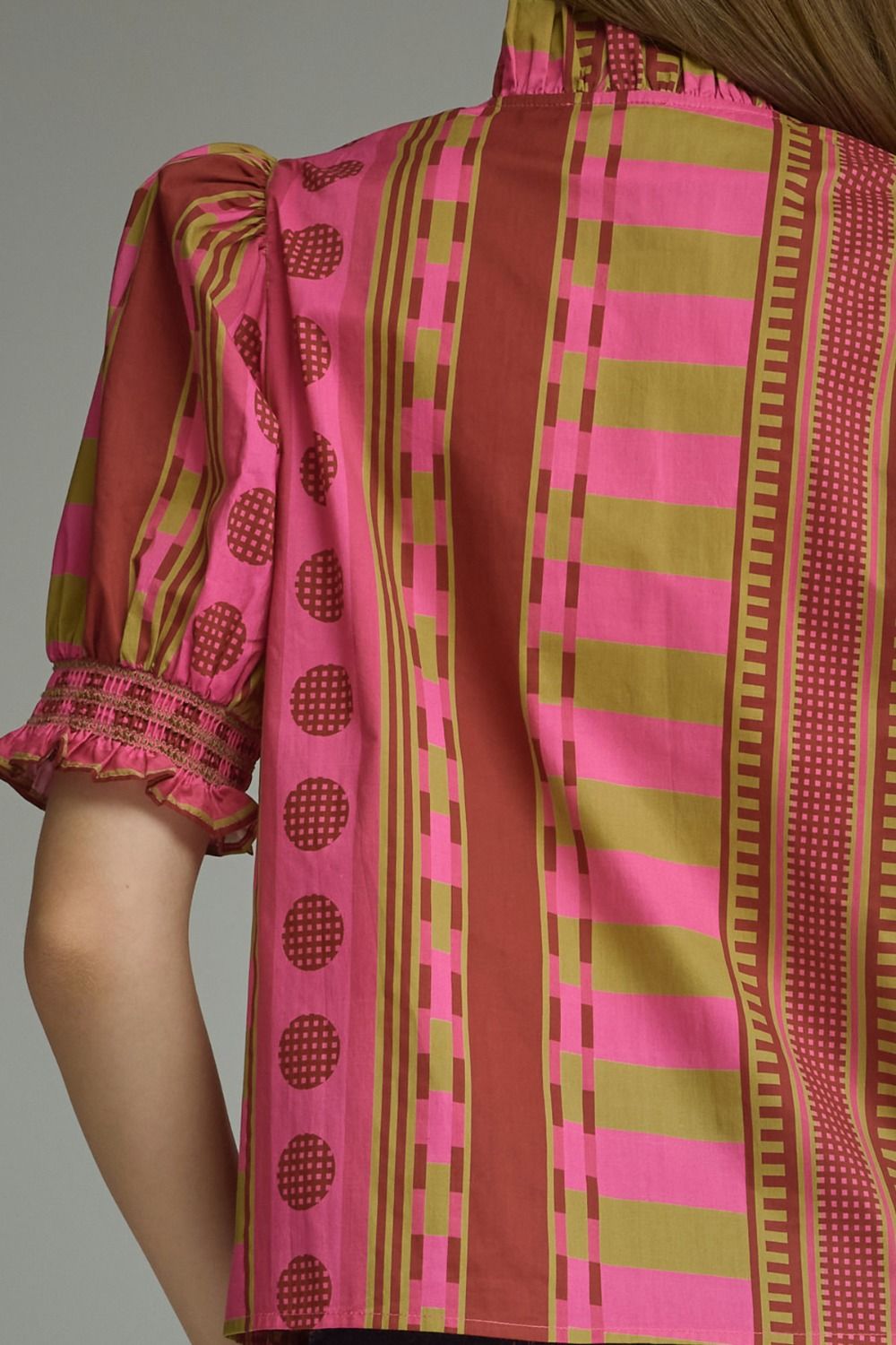 Back view of a pink and olive mixed print top with short puff sleeves and a ruffled high neck.