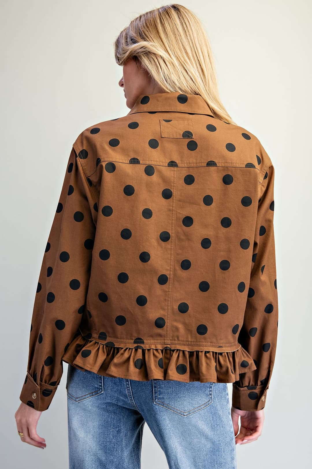 Back view of a brown polka dot button-down blouse with a ruffled hem and long sleeves.