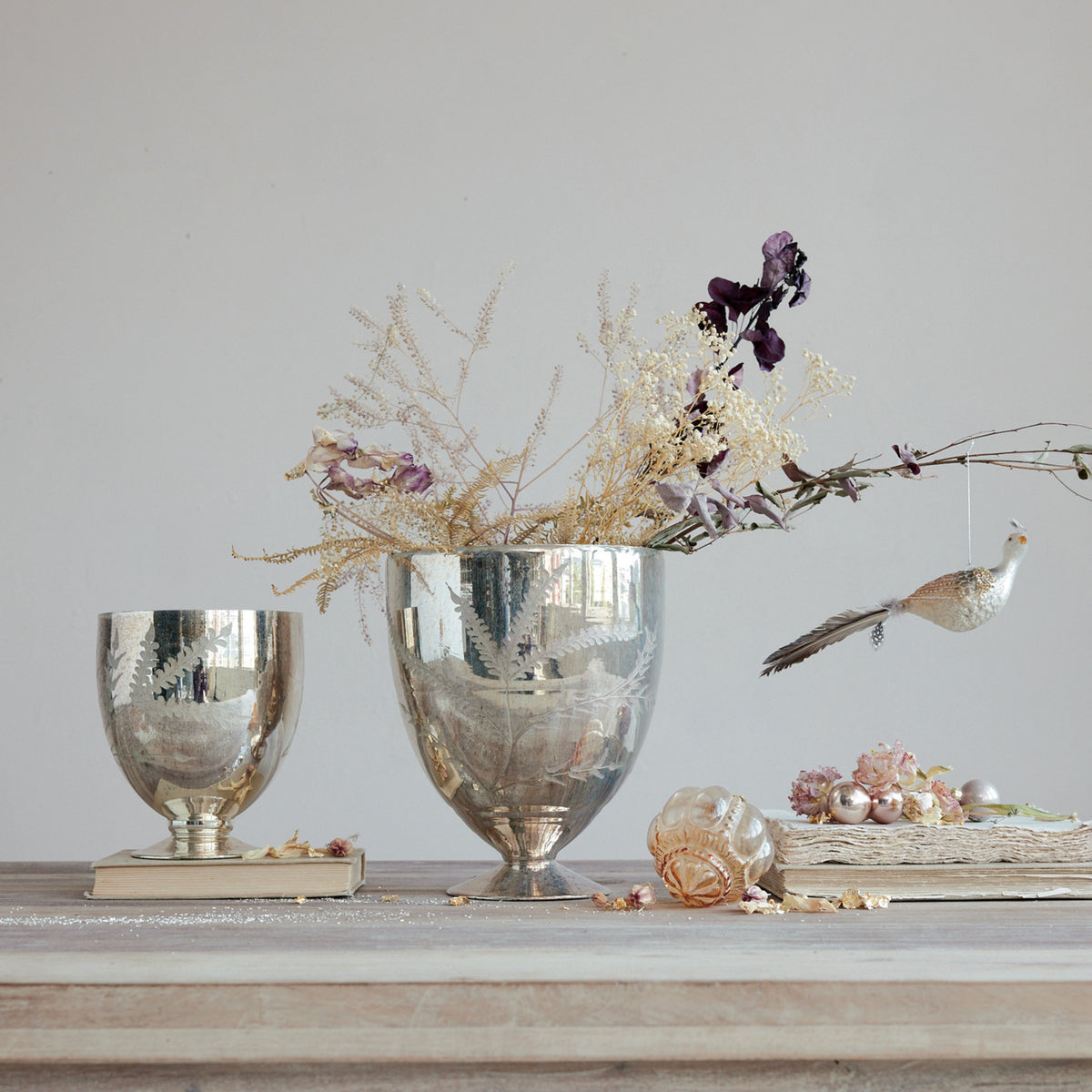 Two etched mercury glass footed vases with an antique silver finish on a wooden table.