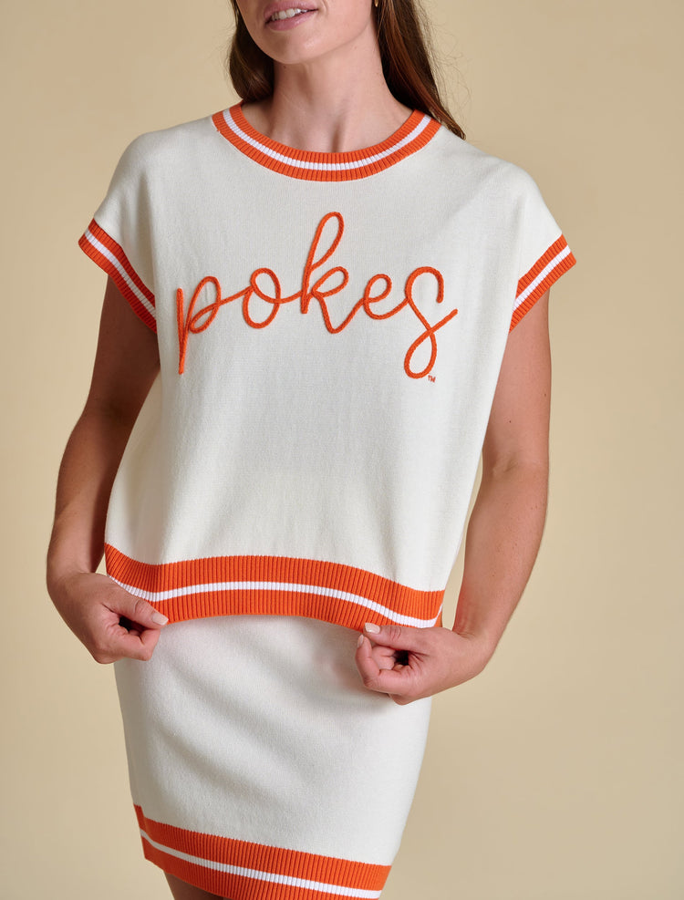 White sleeveless varsity sweater with orange 'pokes' embroidery and striped trim.