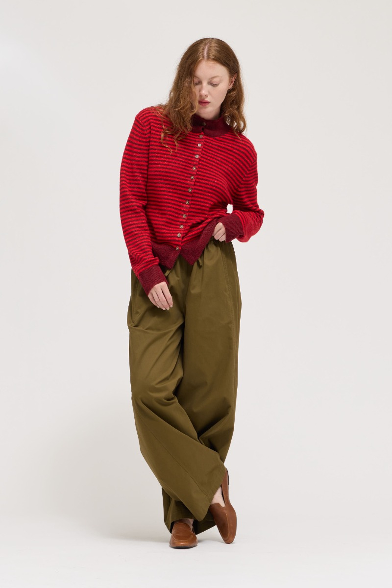 Woman wearing a red and burgundy striped mock neck sweater cardigan with olive green trousers.
