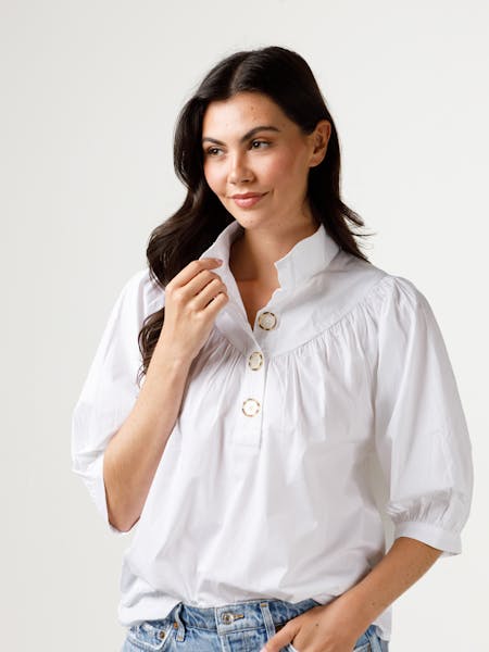 Woman wearing the white Avie Top with a stand collar, three buttons, and puff sleeves.